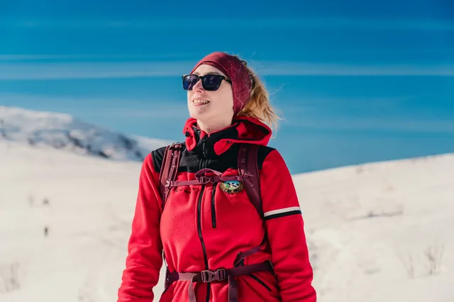 Portrait of a hiker wearing a red jacket and sunglasses in snow.