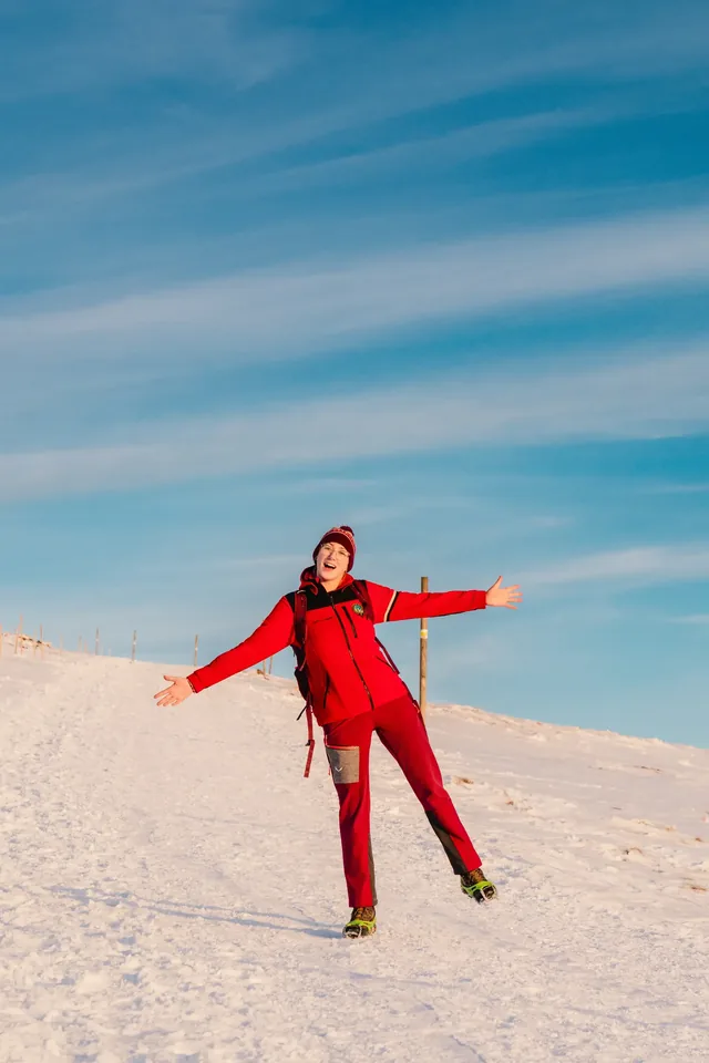 Hiker in red with arms outstretched on snow.