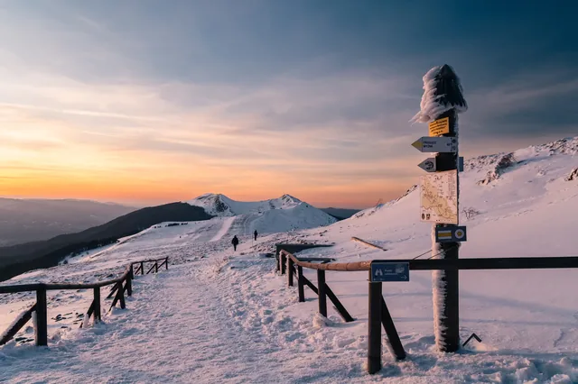 Snow-covered fence and signpost beneath a colourful sky.