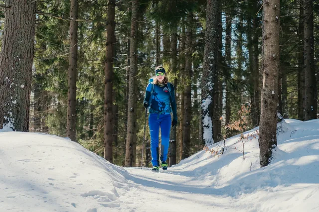Hiker in blue trousers on a path in a winter forest.