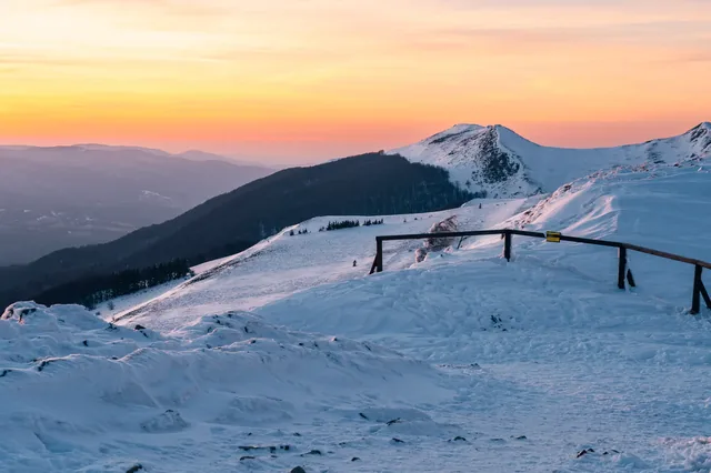 Snowy ridge and fence beneath a pink sky.