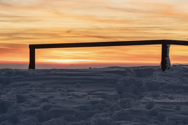 Wooden railing and snow beneath a golden sky.