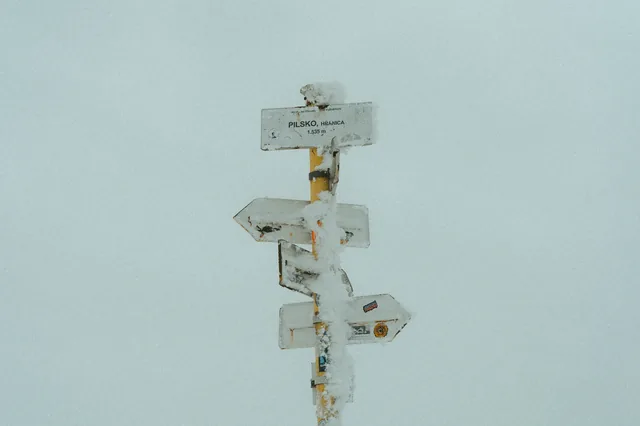 Ice-covered arrows on a winter trail signpost.
