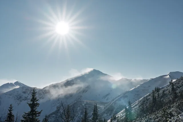Sun above a snowy mountain range and forest.