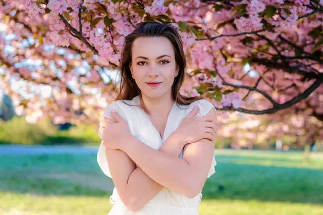 Portrait with crossed arms beneath pink flowering branches.