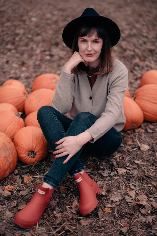 Woman sitting among orange pumpkins and fallen leaves.