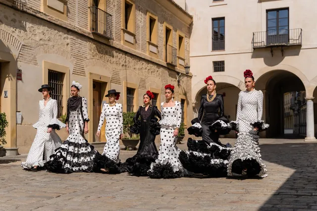Group in dresses and hats in a cobbled square.