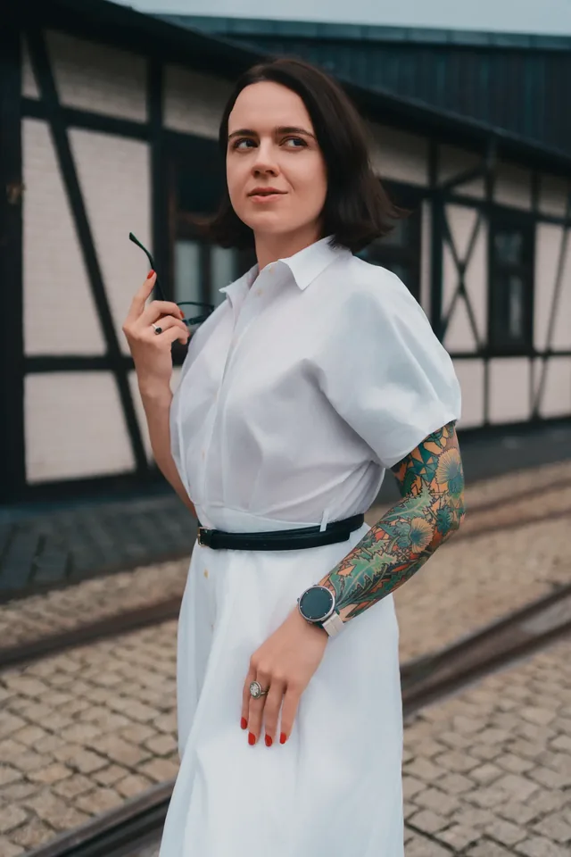 Woman in a white dress beside a timber-framed building.