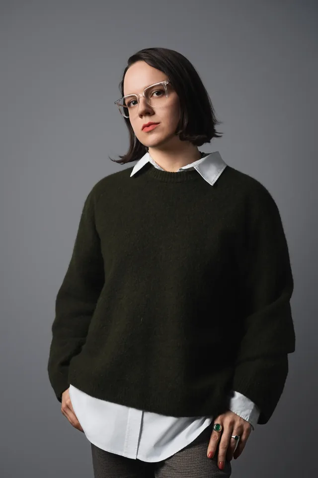 Studio portrait in a dark jumper and white shirt.