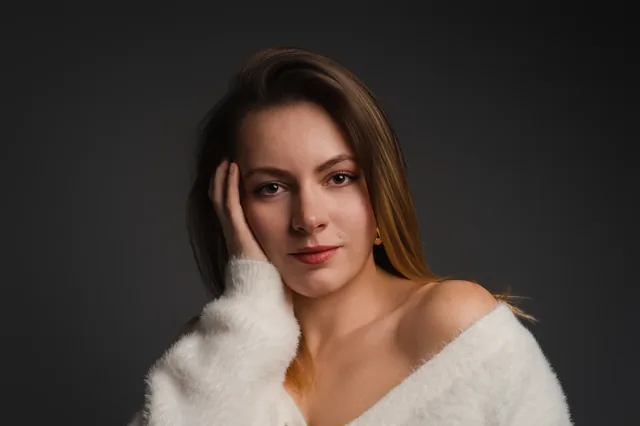 Portrait in a pale jumper with a hand beside the hair.