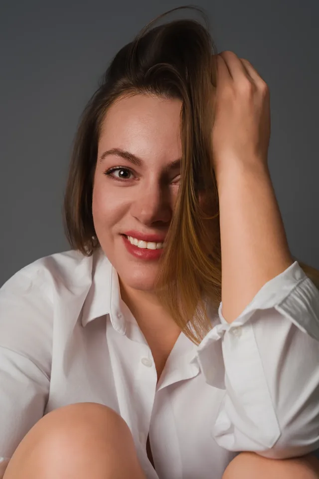 Smiling woman in a white shirt with a hand beside her head.