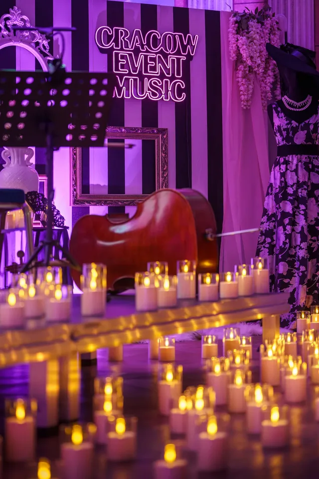 Candles and a cello in front of a concert banner.