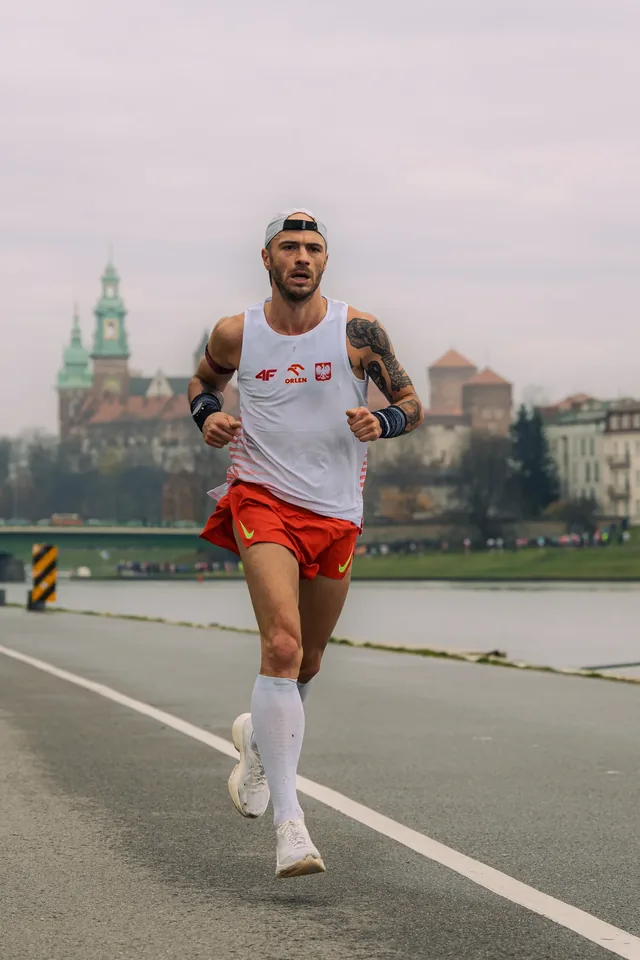 Runner in a white vest and red shorts beside a river.