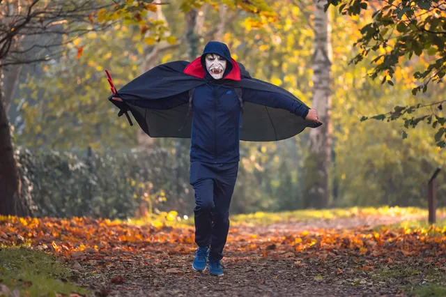 Person in a dark cape with arms outstretched on a path.