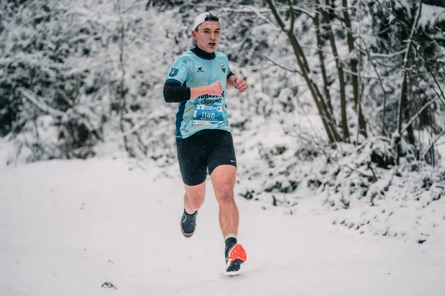 Runner in a turquoise shirt on a snow-covered track.