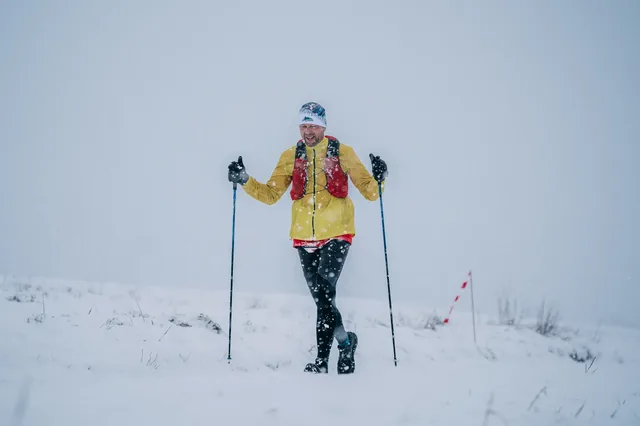 Runner in a yellow jacket with poles in a winter landscape.