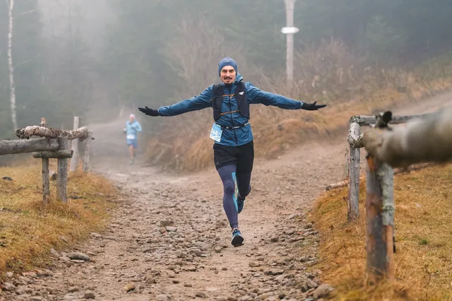 Runner in blue with outstretched arms on a stony track.