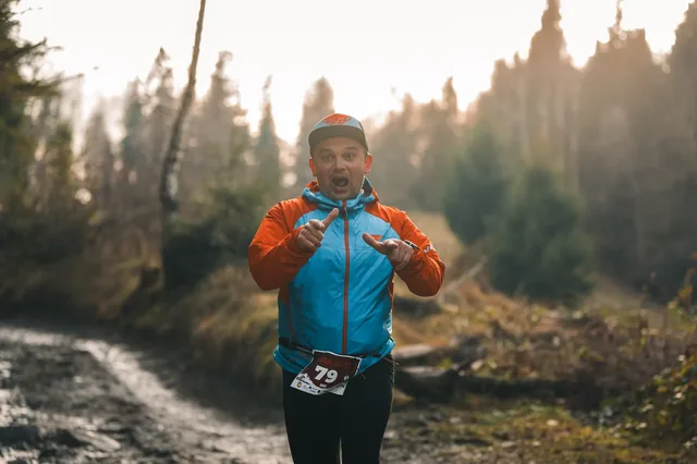 Runner in a blue and orange jacket on a forest track.