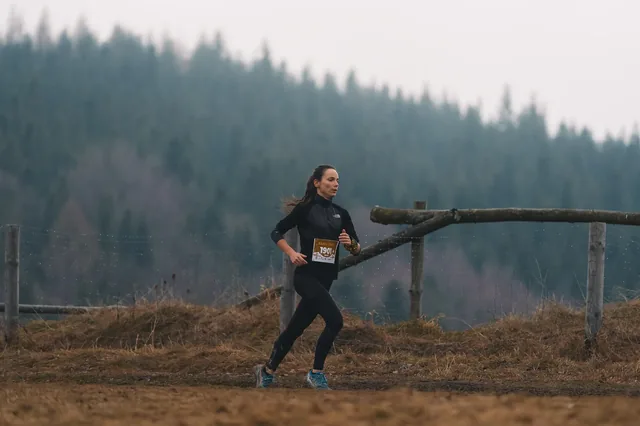 Runner in black beside a hillside fence.