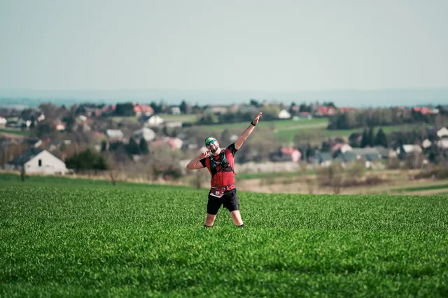 Runner with a raised arm in a green field with buildings behind.