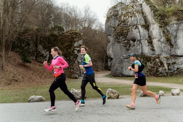 Runners in pink and green tops on a paved road.