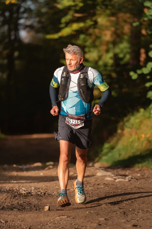 Runner with a backpack in side light on a forest track.