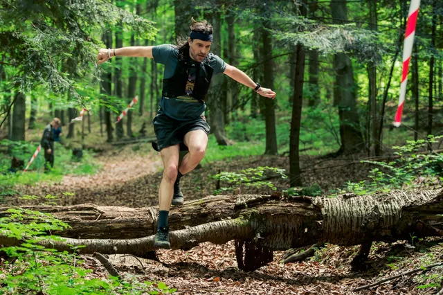 Runner jumping over a fallen log on a forest trail.