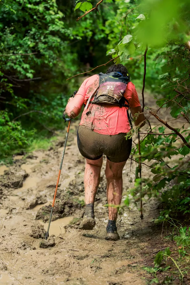 Participant with a red backpack on a steep forest climb.